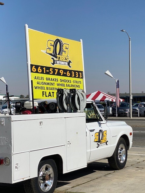 The S.O.S. Tires service truck with its yellow signboard listing axles, brakes, shocks, struts, alignment, wheel balancing, wheel bearings, oil and flat repair