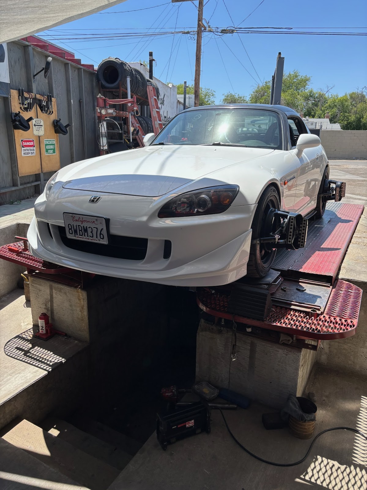 A white Honda S2000 up on the alignment rack at S.O.S. Tires with alignment heads clamped to the wheels
