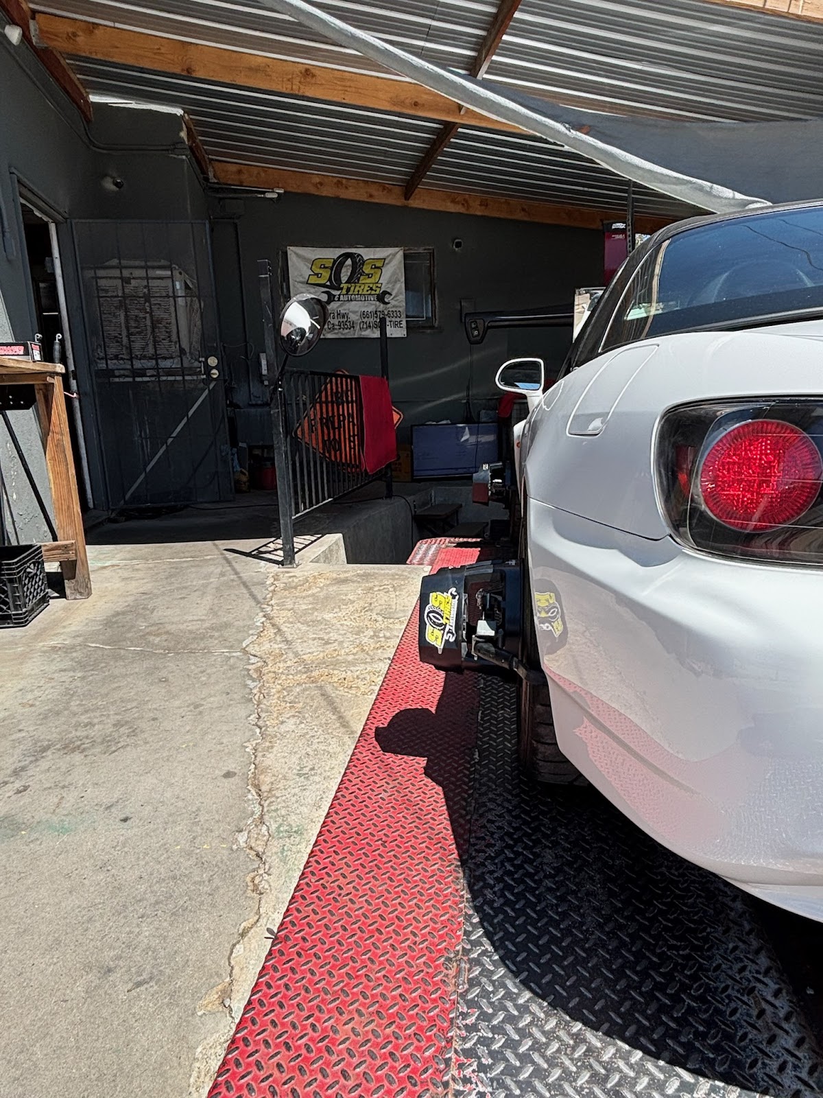 A car under the canopy at S.O.S. Tires beside the shop banner showing both phone numbers
