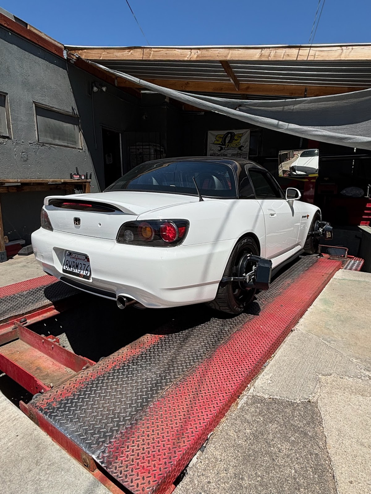 A white Honda S2000 on the alignment ramps at S.O.S. Tires with the shop banner behind
